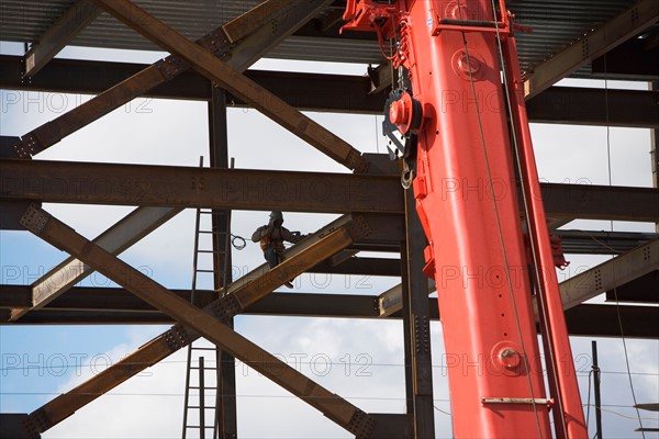 Construction worker working on unfinished structure, red crane in foreground. Photo: fotog