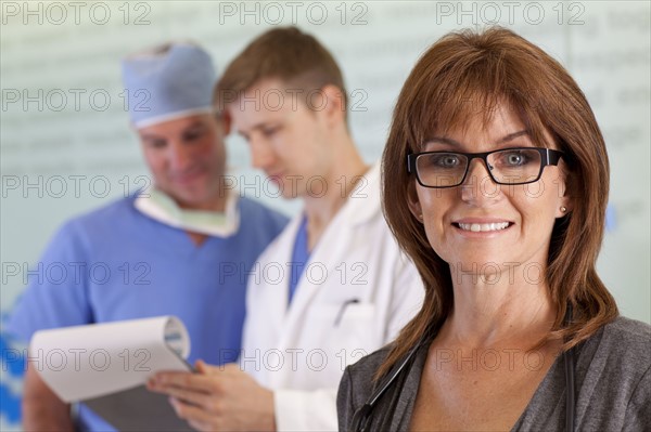 Portrait of female doctor, male doctor and surgeon in background. Photo: db2stock