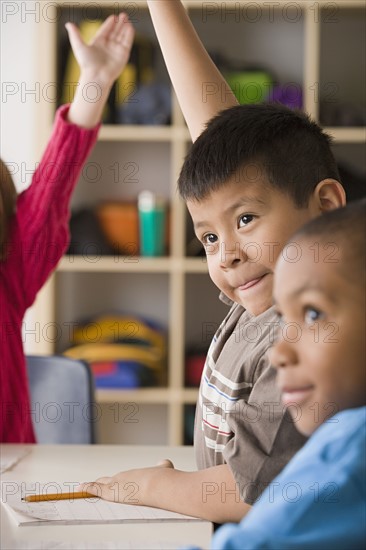 Children (6-7) raising hands in classroom. Photo: Rob Lewine