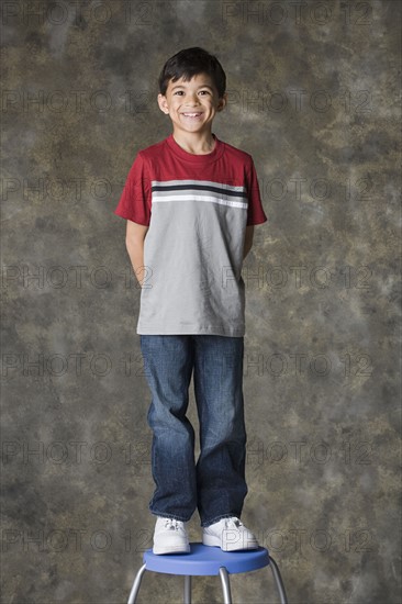 Portrait of smiling boy (8-9) standing on stool, studio shot. Photo: Rob Lewine
