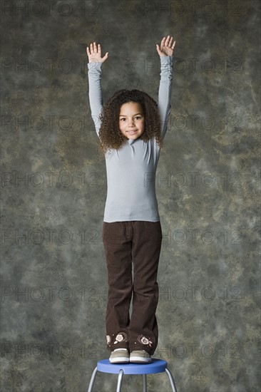 Portrait of smiling girl (8-9) with arms raised, studio shot. Photo: Rob Lewine