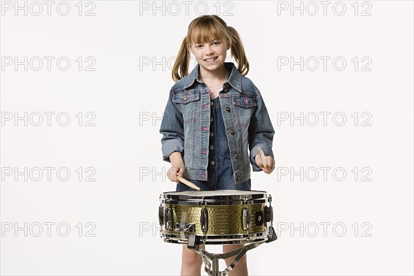 Studio portrait of girl (8-9) playing drums. Photo : Rob Lewine