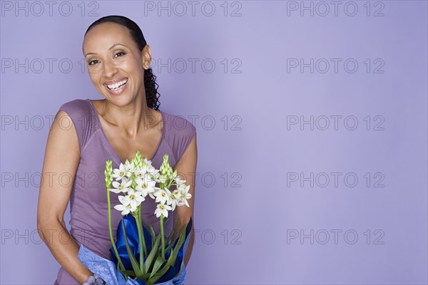 Portrait of smiling woman holding flowers on purple background, studio shot. Photo: Rob Lewine