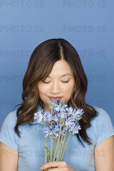 Portrait of woman smelling flowers on blue background, studio shot. Photo: Rob Lewine