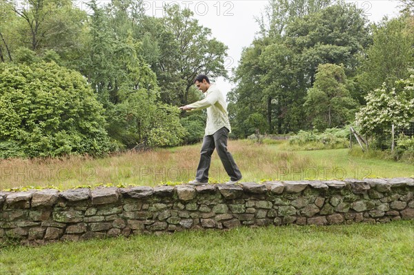 USA, New Jersey, Man walking on stone wall on field. Photo: Tetra Images