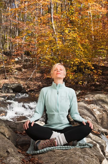 Woman meditating by stream in forest. Photo: Tetra Images