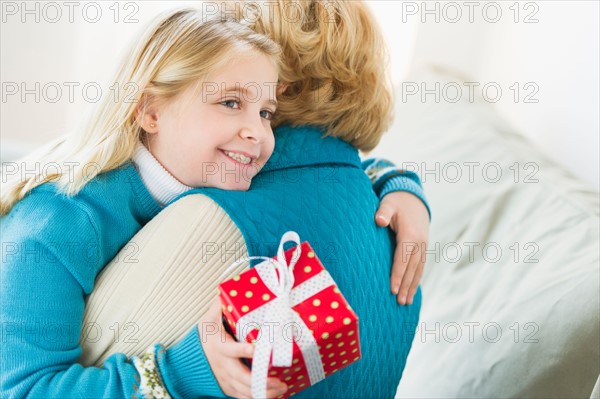 Granddaughter (8-9) hugging grandmother and holding gift.