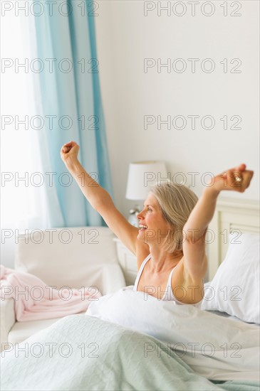 Senior woman stretching in bedroom in morning.