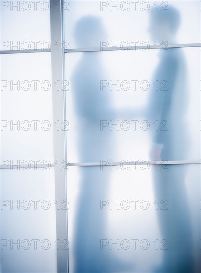 Silhouettes of two businessmen behind glass door.