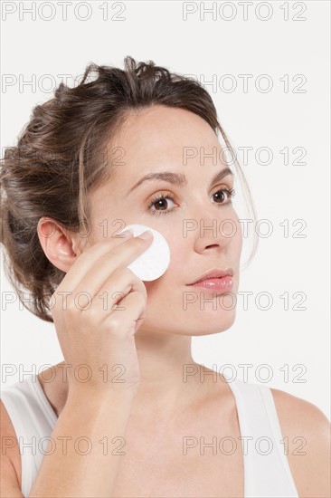 Portrait of woman touching face with cotton pad, studio shot. Photo : Jan Scherders