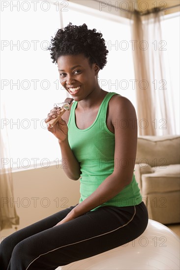 Woman sitting on fitness ball eating chocolate bar. Photo : Rob Lewine