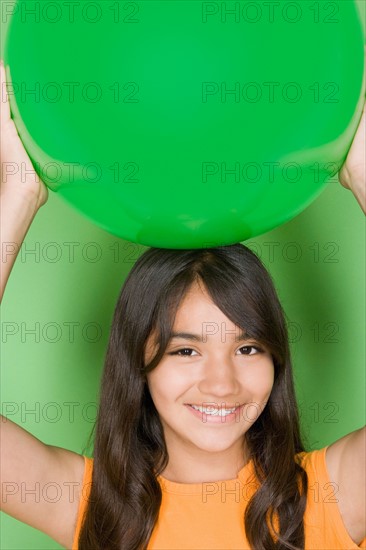 Studio shot portrait of teenage girl holding ball on her head, head and shoulders. Photo : Rob Lewine
