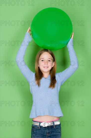 Studio shot portrait of teenage girl holding ball on her head, waist up. Photo : Rob Lewine