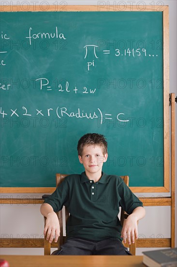 boy sitting in teachers chair, blackboard in background. Photo : Rob Lewine