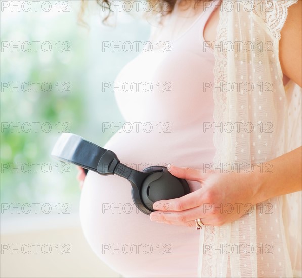 Portrait of pregnant woman holding headphones on her belly. Photo : Daniel Grill