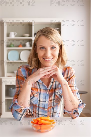 Portrait of mid adult woman with bowl of carrots. Photo : Rob Lewine