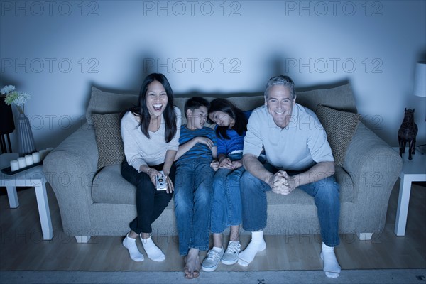 Family sitting on sofa and watching television. Photo : Rob Lewine