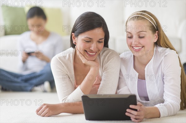 Girls (14-19) lying on floor using tablet pc.