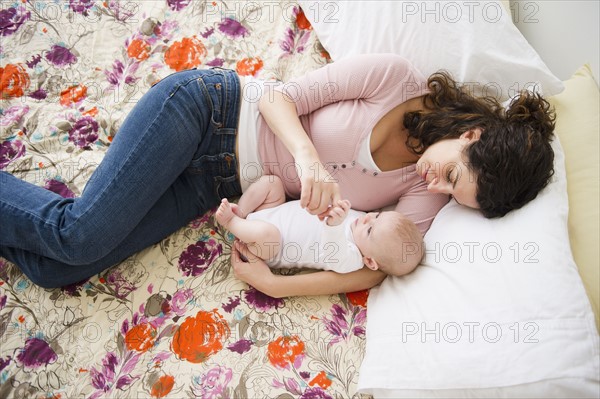 Mother and baby boy (2-5 months) lying together on bed. Photo: Jamie Grill