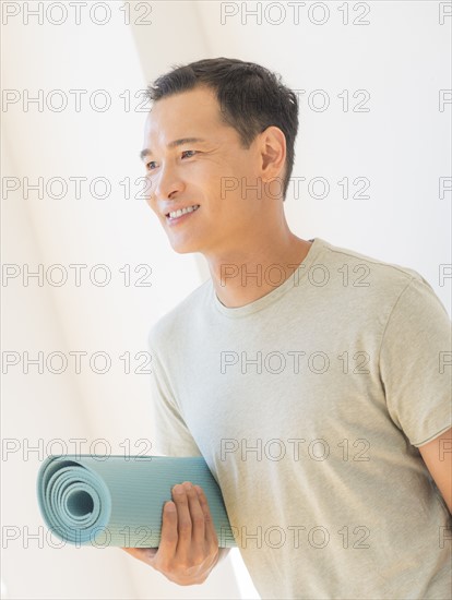 Happy mid adult man holding exercising mat. Photo: Daniel Grill