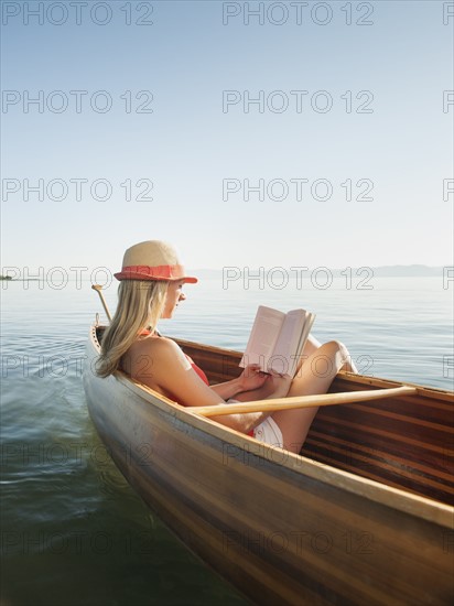 Young woman relaxing in canoe, and reading book. Photo: Erik Isakson