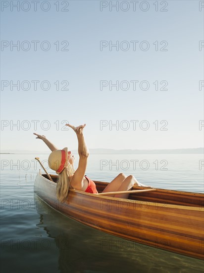 Young woman relaxing in canoe with arms raised. Photo: Erik Isakson
