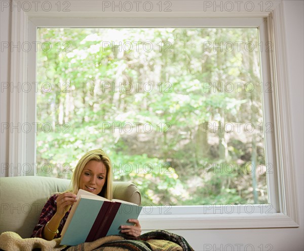 Woman sitting on sofa and reading book. Photo: Jamie Grill