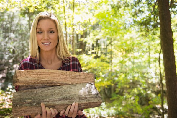 Portrait of woman holding logs in forest. Photo: Jamie Grill