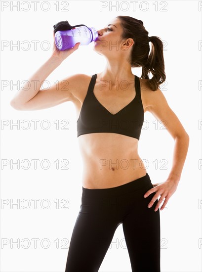 Young woman drinking water after exercising, studio shot. Photo: Mike Kemp