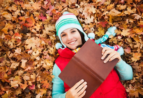 Portrait of young woman with book lying on autumn leaves . Photo: Mike Kemp