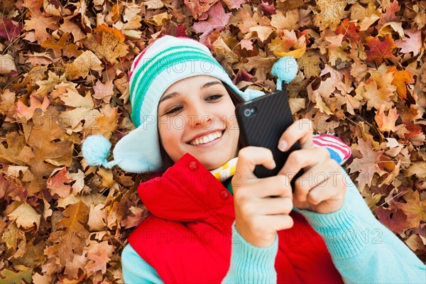 Young woman lying on autumn leaves and using . Photo: Mike Kemp