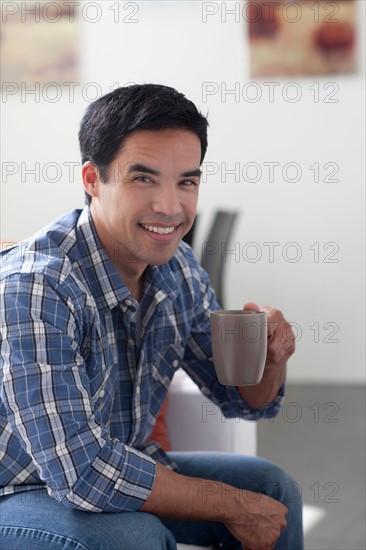 Portrait of man drinking coffee in living room. Photo: Dan Bannister