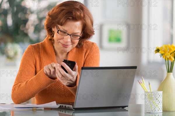 Senior woman working on laptop and text messaging.