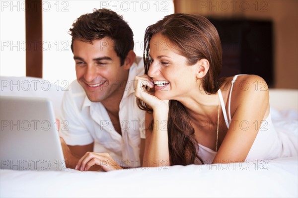 Couple using laptop while lying in bed