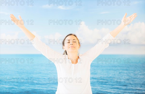 Portrait of woman with arms raised in front of backdrop with sea and sky