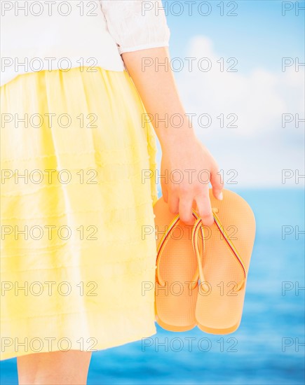 Studio Shot Mid section of woman holding flip-flops, rear view