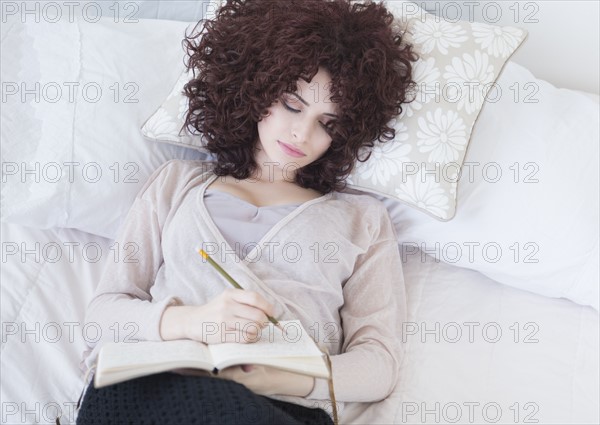 Beautiful woman lying in bed writing diary.