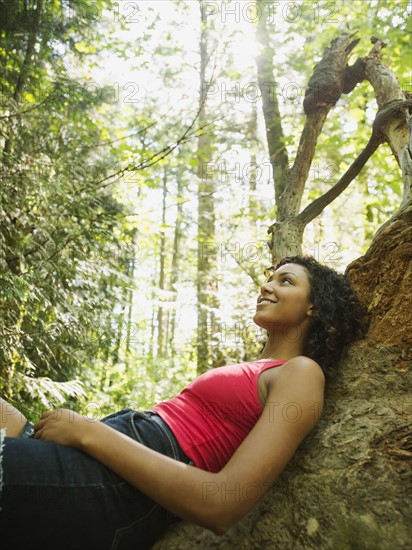 Young woman sitting on log in forest. USA, Oregon, Portland.