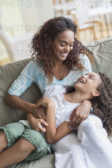 Mother tickling daughter (8-9) on sofa.