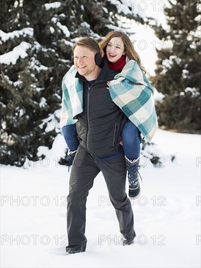 Man giving woman piggyback ride in winter forest