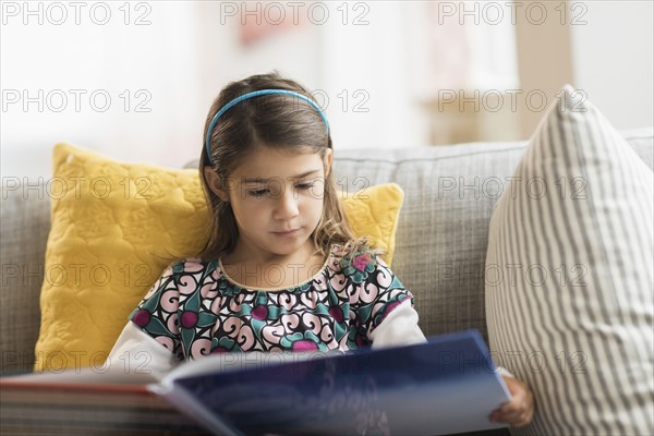 Girl (6-7) reading book at home.