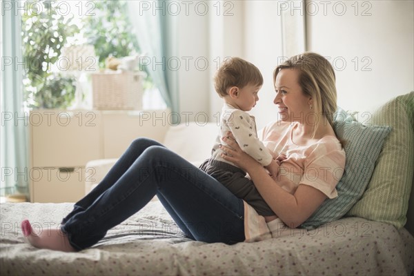 Happy mother playing with little son (2-3 years) on bed.