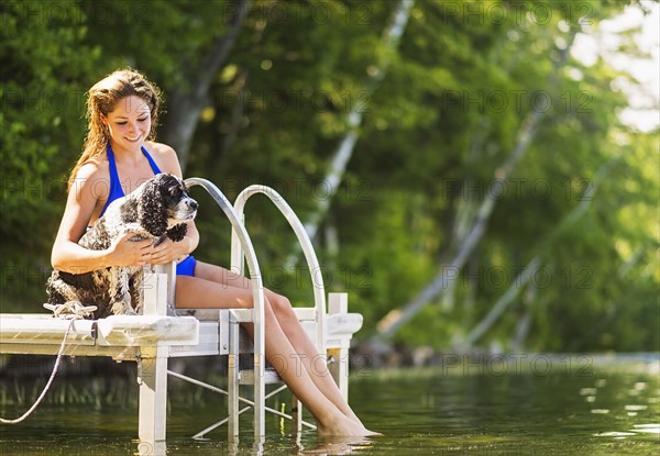 Young woman with dog sitting on jetty over lake