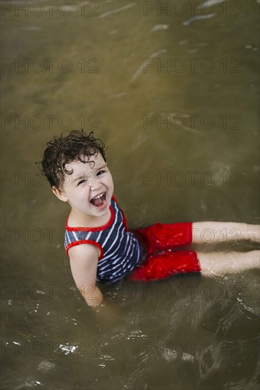 Smiling boy (4-5) sitting in lake