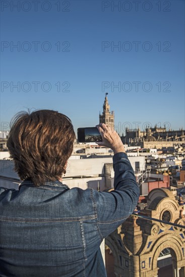 Spain, Andalusia, Seville, Plaza Nueva, Woman taking photo of cityscape and la Giralda with smartphone