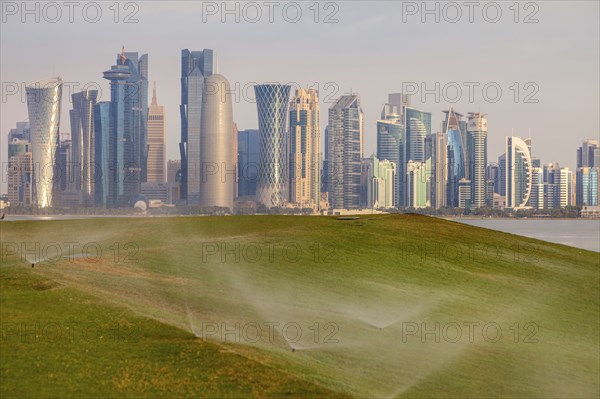 Sprinkler system on lawn by skyline of Doha, Qatar