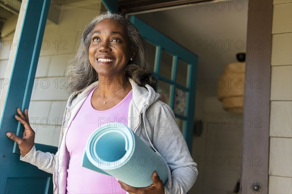 Smiling woman with yoga mat front door