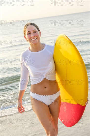 Woman wearing bikini carrying surfboard on beach
