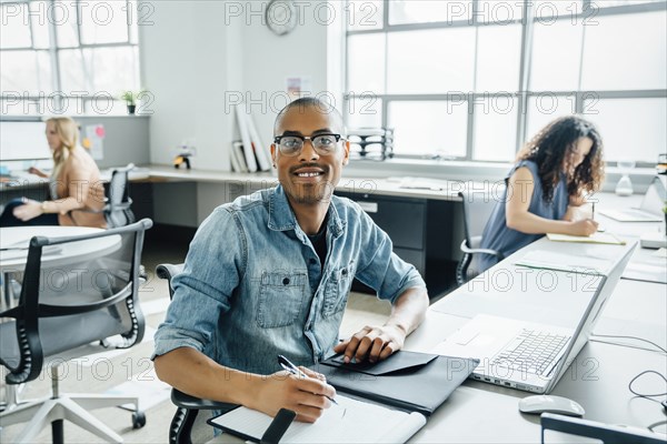 Smiling man using note pad by laptop in office