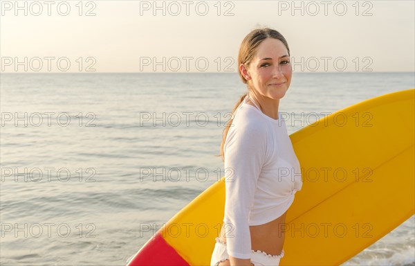 Woman wearing white bikini carrying surfboard on beach